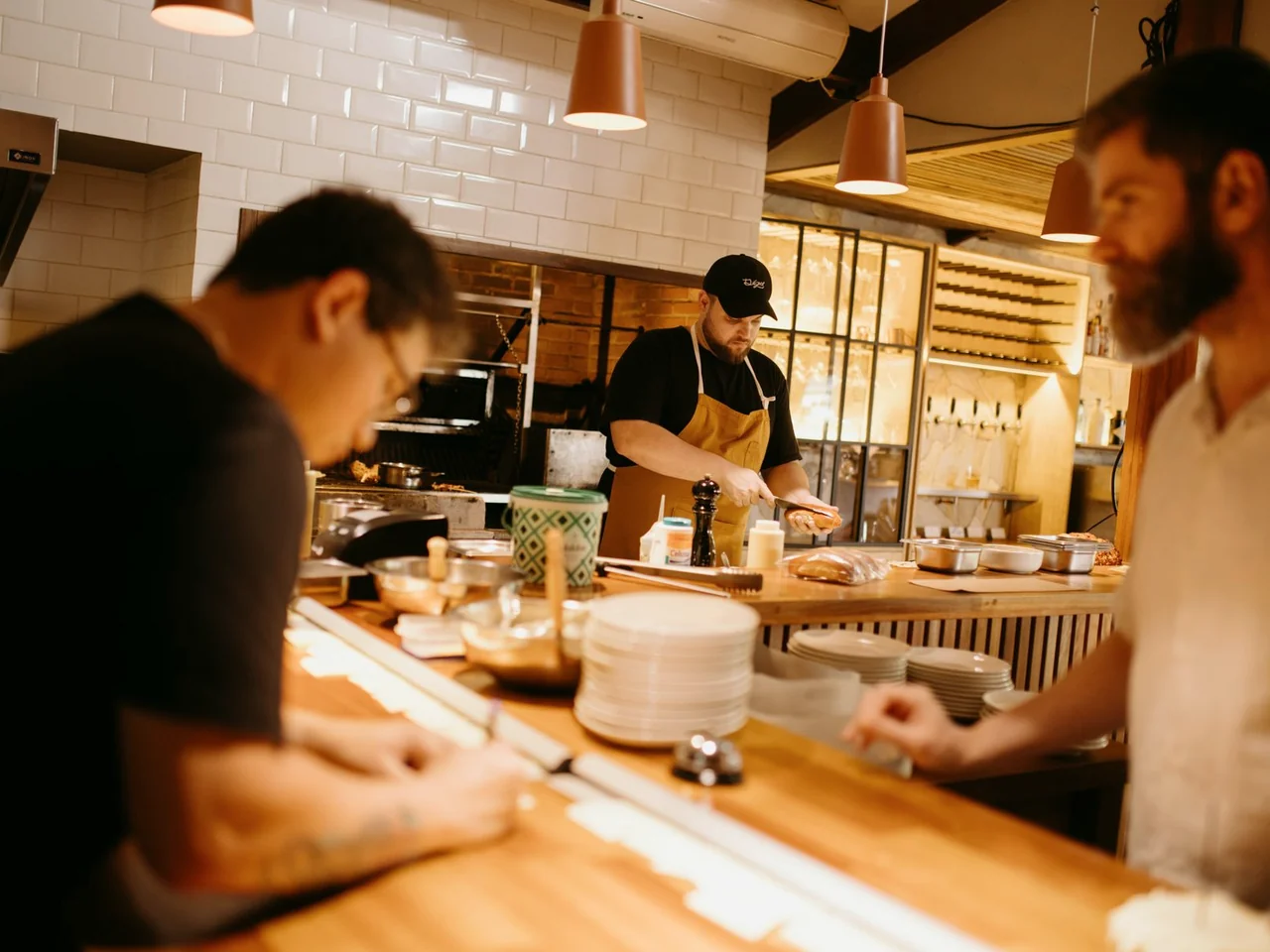 Chefs coordinating preparation across a warmly lit restaurant counter.
